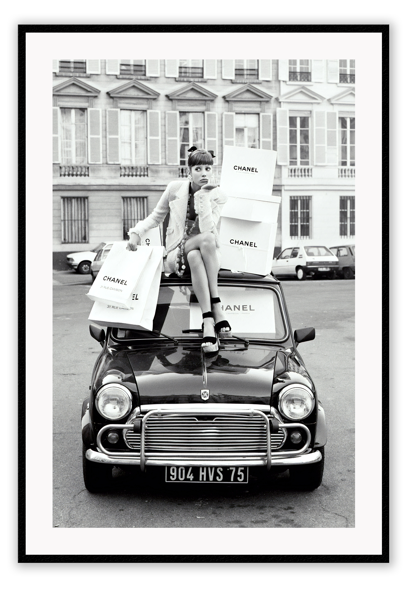 A black and white vintage fashion wall art with a lady holding Chanel shopping bags riding on vintage car Fiat in European city.