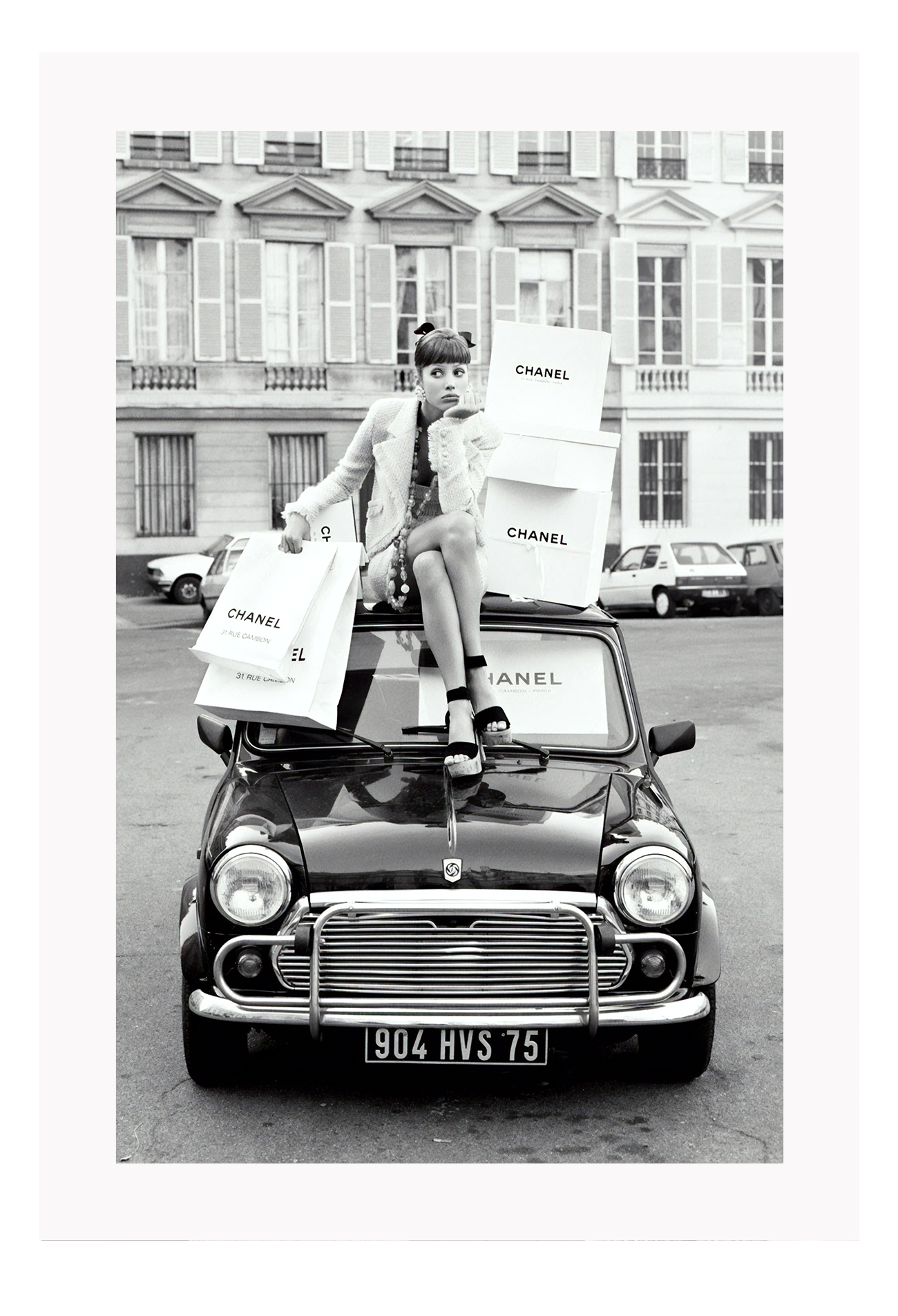 A black and white vintage fashion wall art with a lady holding Chanel shopping bags riding on vintage car Fiat in European city.