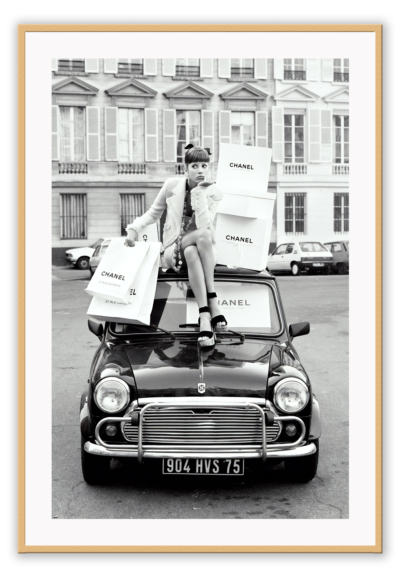 A black and white vintage fashion wall art with a lady holding Chanel shopping bags riding on vintage car Fiat in European city.