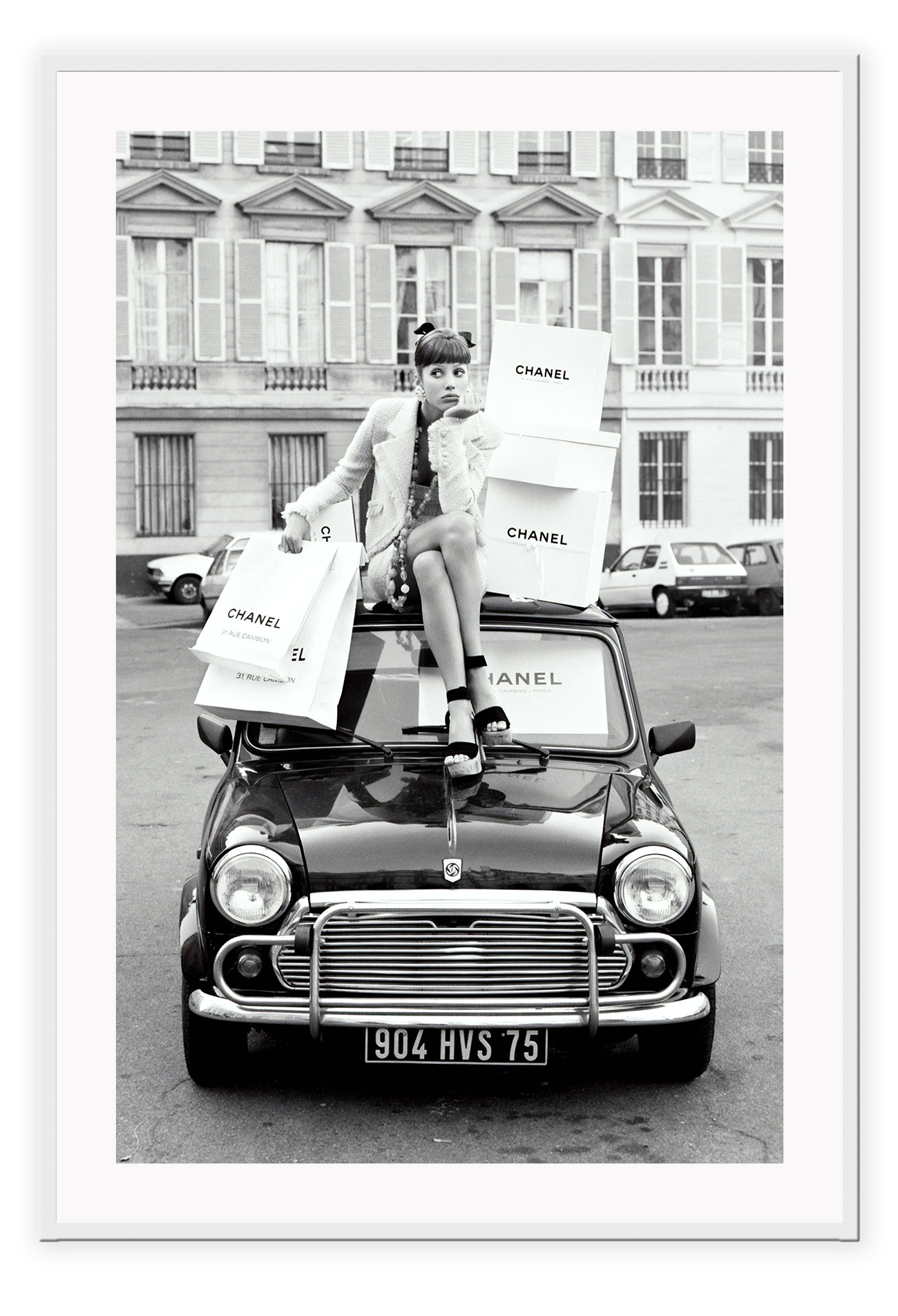 A black and white vintage fashion wall art with a lady holding Chanel shopping bags riding on vintage car Fiat in European city.