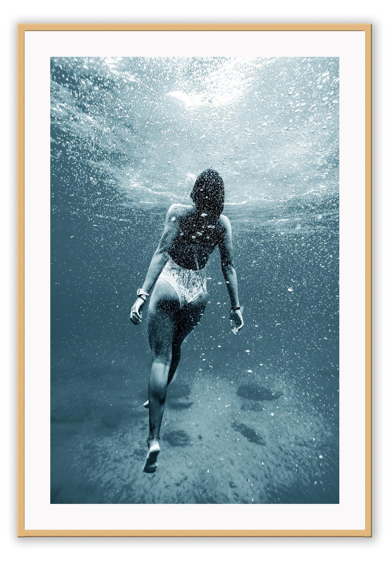 Photography of woman swimming in blue sea water looking up towards the surface pointed toes bubbles