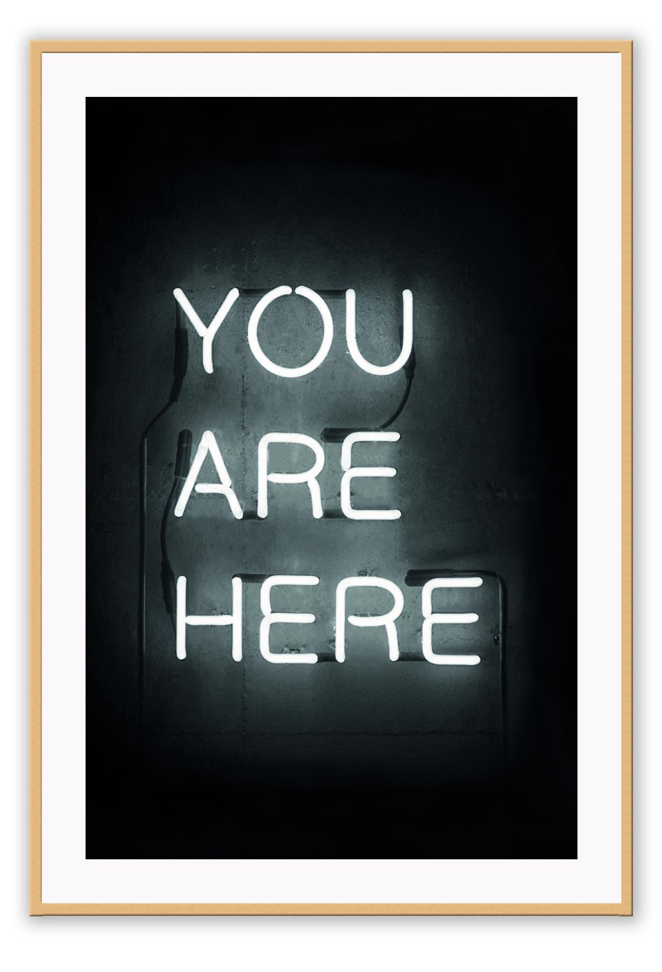 A black and white, scandi typography wall art with YOU ARE HERE neon letter lighting installation on a black wall background.