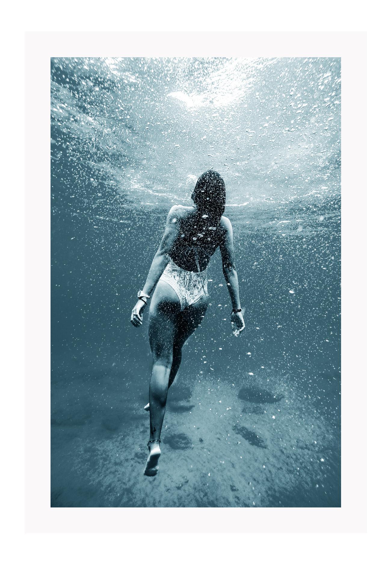 Photography of woman swimming in blue sea water looking up towards the surface pointed toes bubbles