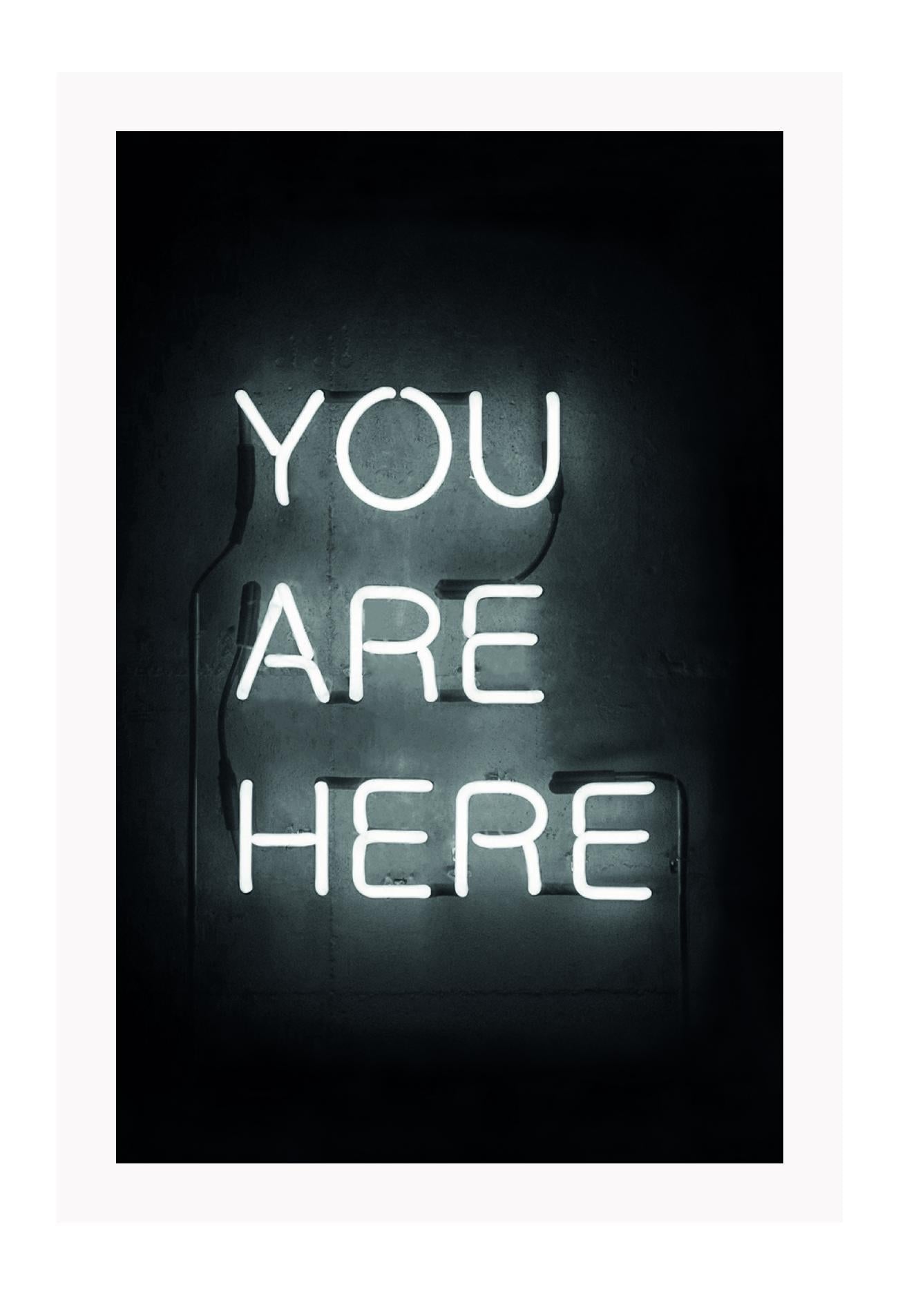 A black and white, scandi typography wall art with YOU ARE HERE neon letter lighting installation on a black wall background.