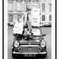 A black and white vintage fashion wall art with a lady holding Chanel shopping bags riding on vintage car Fiat in European city. 