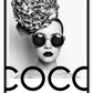 A black and white fashion photographic wall art of a lady holding balloon leaning on a scandi bike, riding on the writing coco chanel I don't do fashion I am fashion. 