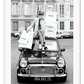 A black and white vintage fashion wall art with a lady holding Chanel shopping bags riding on vintage car Fiat in European city. 