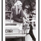 A black and white photo print of a fashion model woman lady on vintage car patting dog dachshund blonde and sexy 