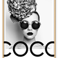 A black and white fashion photographic wall art of a lady holding balloon leaning on a scandi bike, riding on the writing coco chanel I don't do fashion I am fashion. 