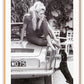 A black and white photo print of a fashion model woman lady on vintage car patting dog dachshund blonde and sexy 