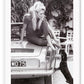 A black and white photo print of a fashion model woman lady on vintage car patting dog dachshund blonde and sexy 
