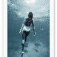 Photography of woman swimming in blue sea water looking up towards the surface pointed toes bubbles 